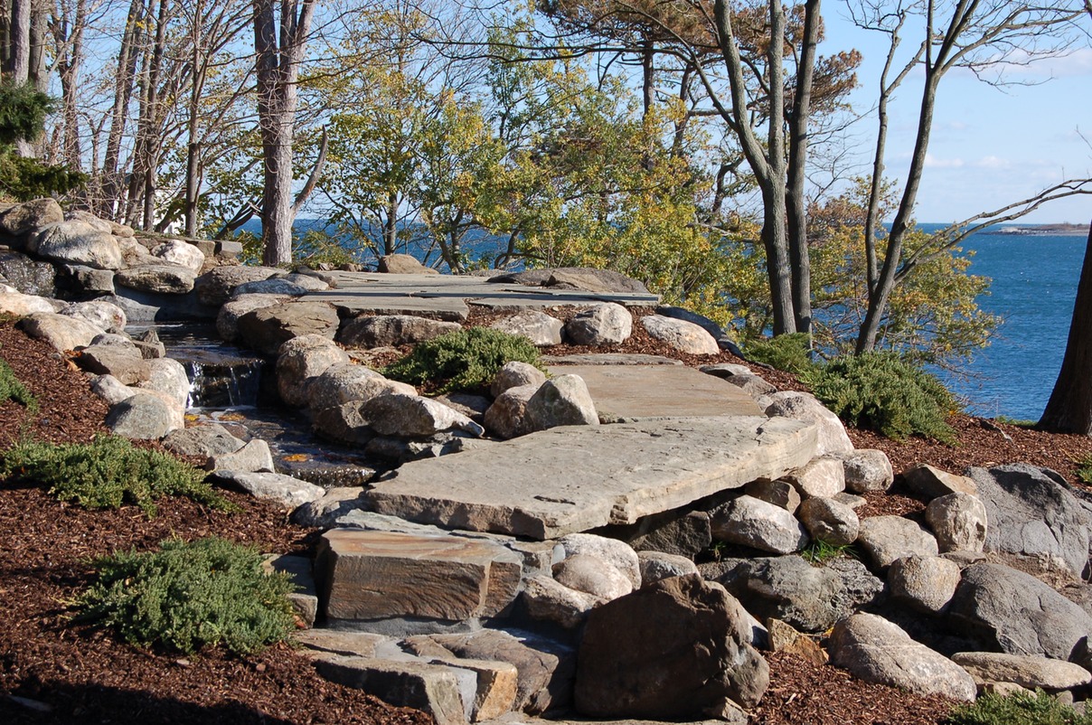 fieldstone stream with path and bridge leading to patio